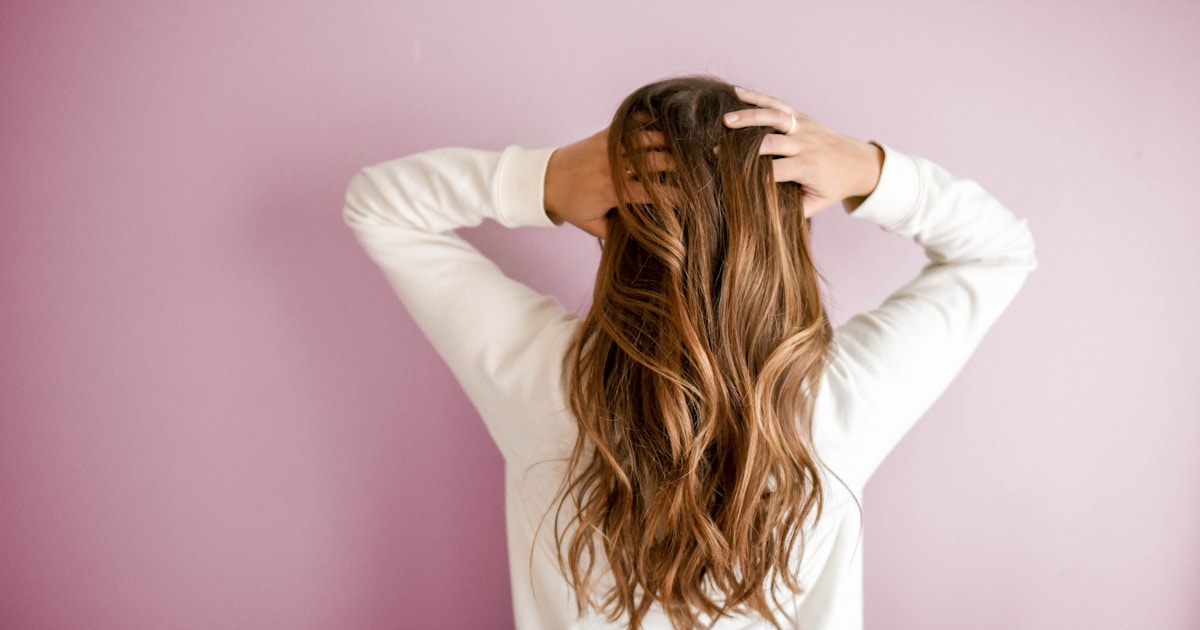 Close-up of healthy thick hair being parted to show scalp, soft natural lighting